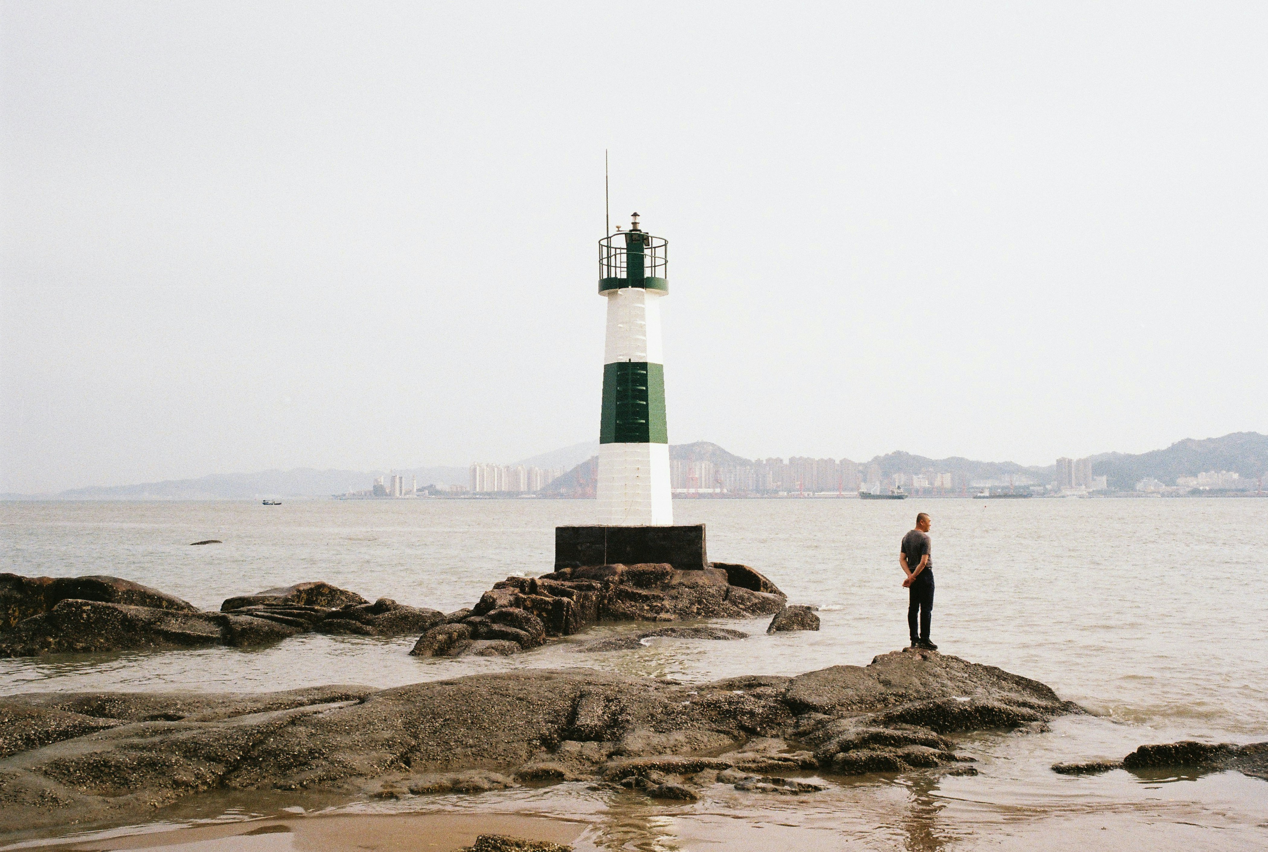 man in black jacket standing on rock near white and red lighthouse during daytime